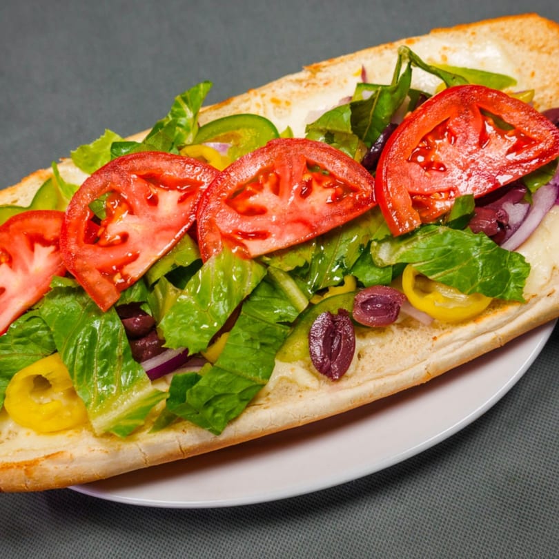 A close-up of a submarine sandwich filled with fresh lettuce, tomatoes, olives, and peppers.