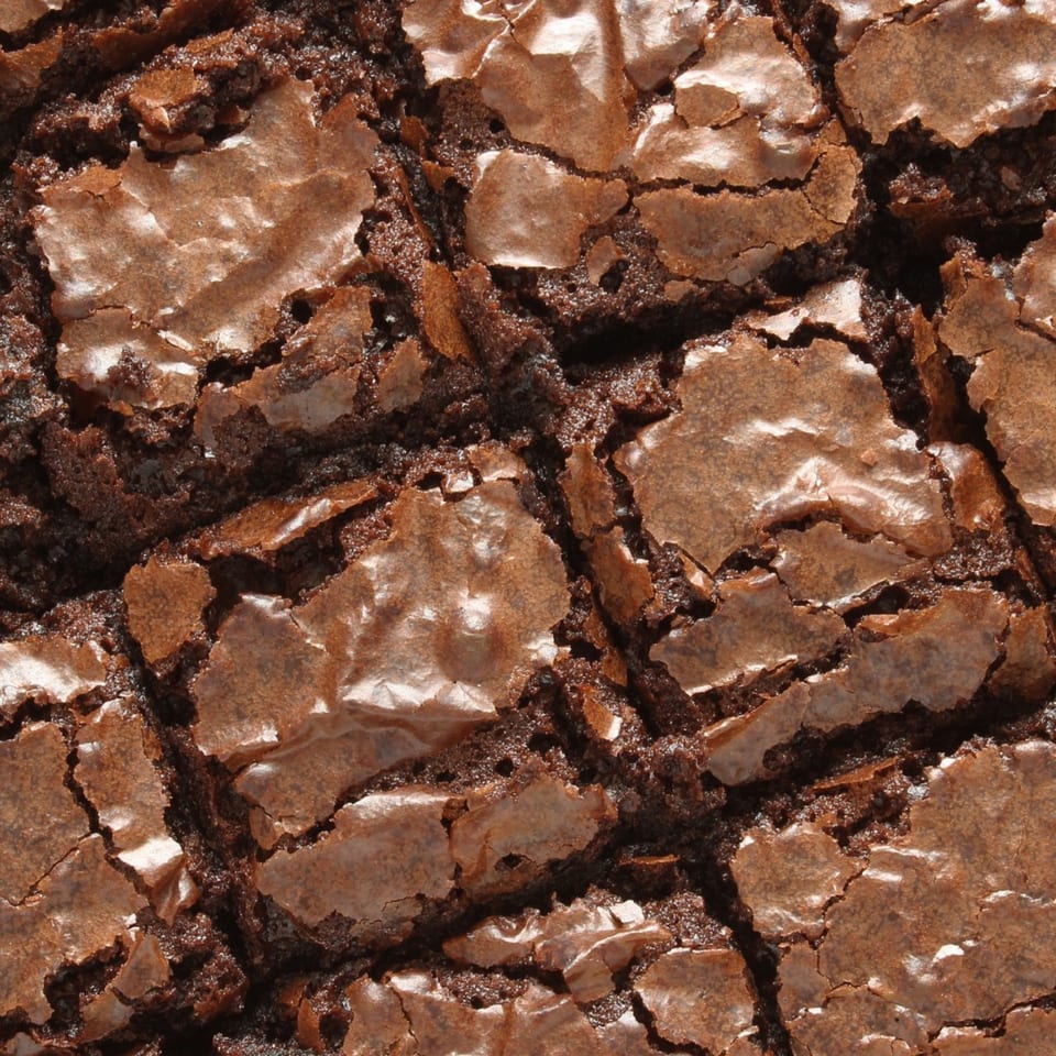 Close-up of a rich, dark chocolate brownie with a cracked, shiny crust.
