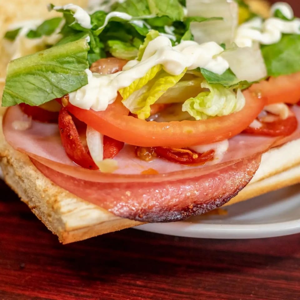 Close-up of a sandwich with ham, tomatoes, lettuce, and mayonnaise on a toasted bun.