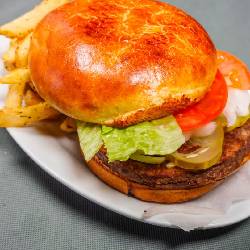 Close-up of a burger with lettuce, tomato, pickles, and onions, served with french fries.