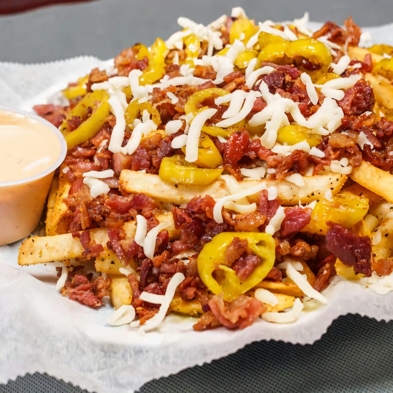 Loaded fries with bacon, shredded cheese, and yellow peppers, with a side of dipping sauce.