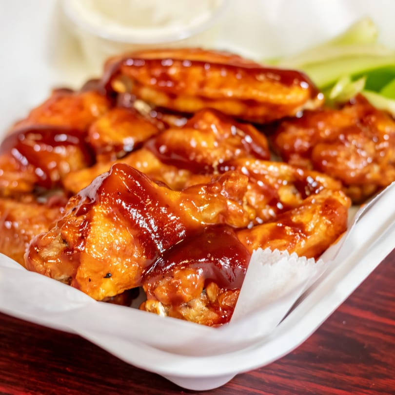A platter of BBQ chicken wings with celery sticks and ranch dressing in the background.