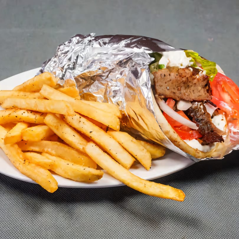 A gyro wrapped in foil with fries on a white plate, against a gray background.